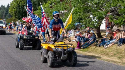 Young riders on ATVs decorated with American flags race down the parade route during the Fourth of July celebration in Home, Washington.